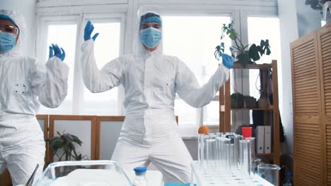 celebrating success. two excited crazy happy female chemical lab doctors in white protection suits do fun dance at work.