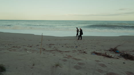 on a long beach, two people walk while watching the fury of the ocean waves