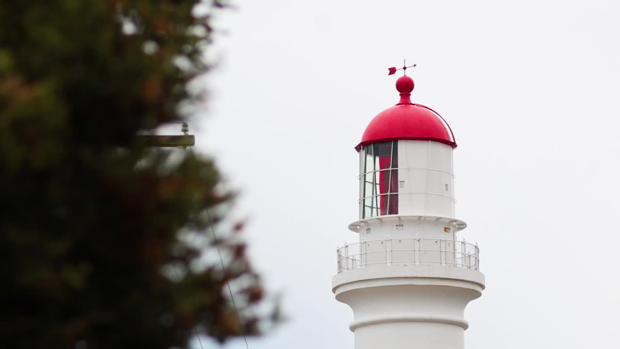 A serene view of Split Point Lighthouse with a red dome, framed by trees, under an overcast sky on Great Ocean Road