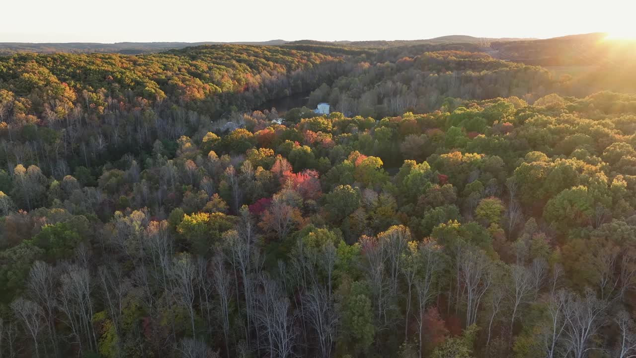 Aerial wide shot of river between colored trees in fall season. Sunset behind mountains in idyllic woodland of America. Peaceful scene