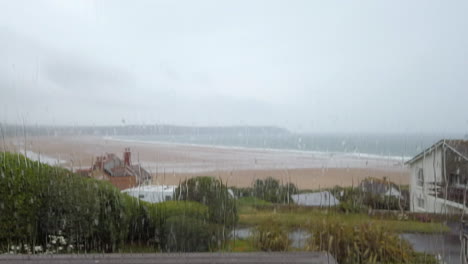 Toma-De-Pedestal-De-Gotas-De-Lluvia-Golpeando-Una-Ventana-De-Vidrio-Con-Vista-Al-Mar-En-Cámara-Lenta