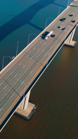 automobile bridge with one-way multi-lane road. transport moving by the bridge over the calm blue water. top view. vertical video