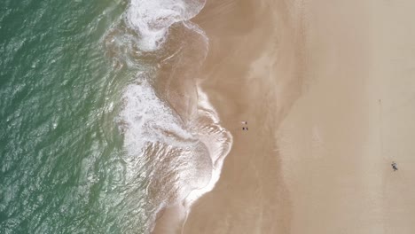 Zwei-Menschen-Legen-Sich-Bäuchlings-In-Die-Nähe-Des-Ufers-Des-Papohaku-Strands-Auf-Maui,-Hawaii,-Sonnen-Sich,-Genießen-Die-Sonnenstrahlen-Und-Lauschen-Dem-Rauschen-Des-Ozeans-–-Luftaufnahme-Von-Oben-Nach-Unten,-Aufwärtsheben