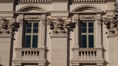 close-up of a historic baroque façade in rome, italy, featuring symmetrical windows, decorative stone carvings, and corinthian capitals illuminated by sunlight.