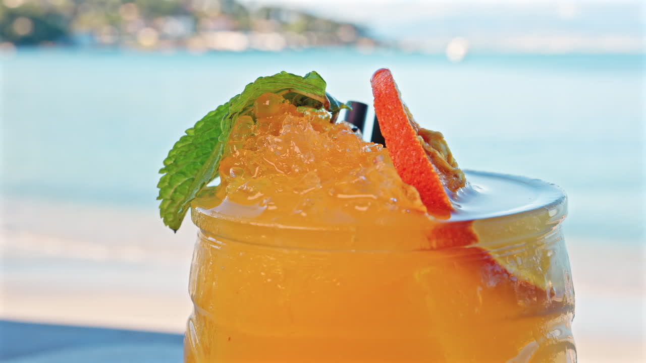 Close up of an orange cocktail on a table with a blurred view of the sea on the background