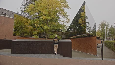 man walking up to sign of national holocaust names memorial in amsterdam, the netherlands and taking photo of reflecting mirrors on the the monument