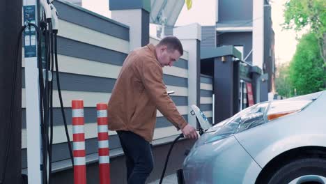 proceso de reabastecimiento de combustible de un automóvil eléctrico. un disparo debajo de la escotilla donde se carga el automóvil ecológico eléctrico. la escotella de carga del automóvil eléctrico se abre automáticamente. una mano masculina inserta un automóvil erecto