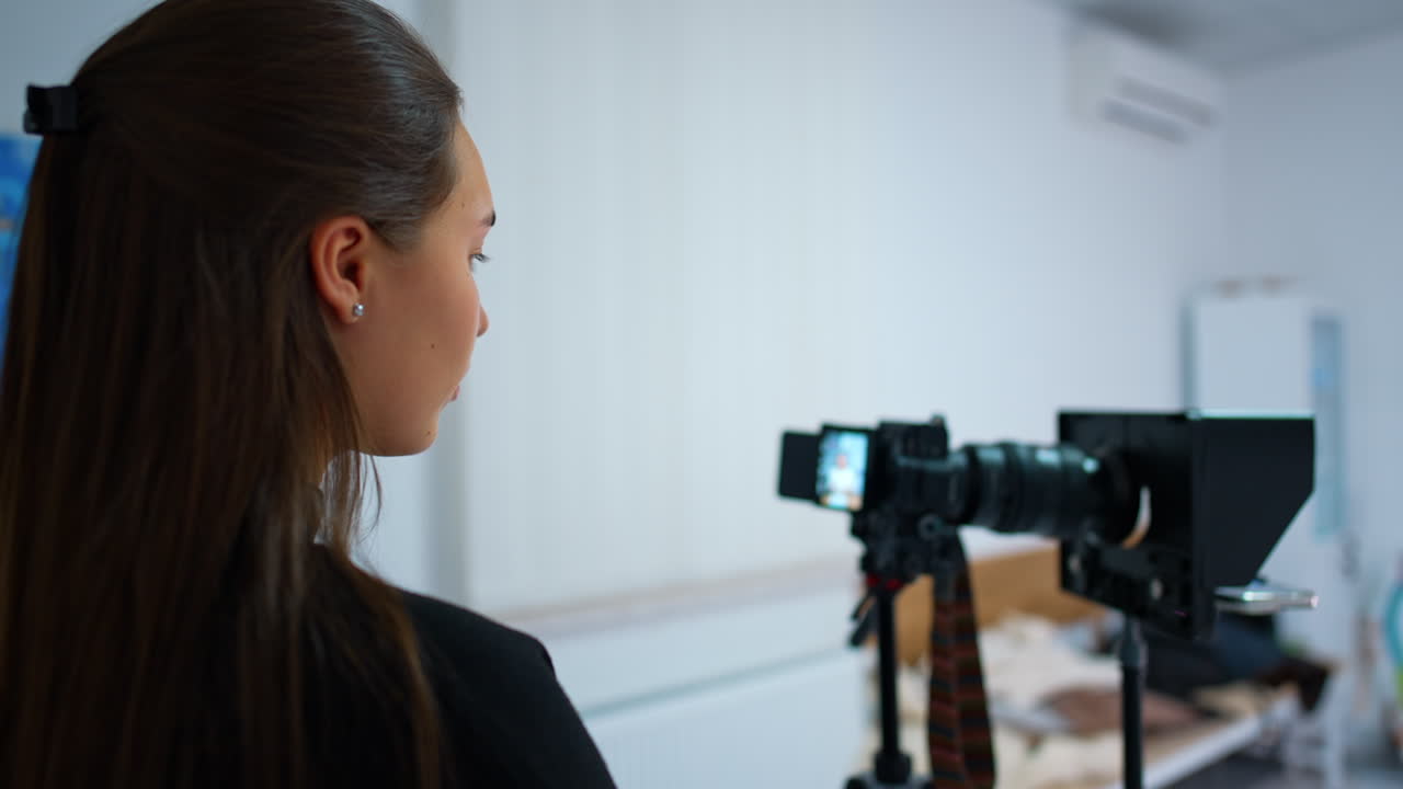 Caucasian brunette looks attentively at the camera display. Girl taking video for the blog content. Blurred backdrop.