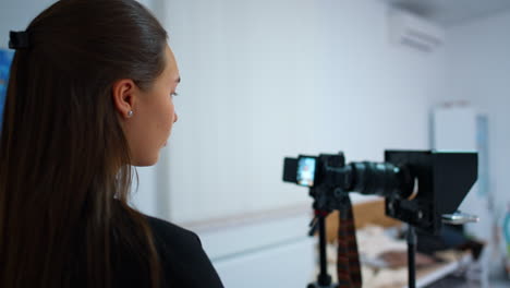 caucasian brunette looks attentively at the camera display. girl taking video for the blog content. blurred backdrop.