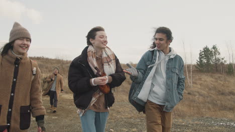 Front-View-Of-Group-Of-Teenage-Friends-Talking-And-Walking-In-A-Wheat-Field-Path-On-A-Windy-Day