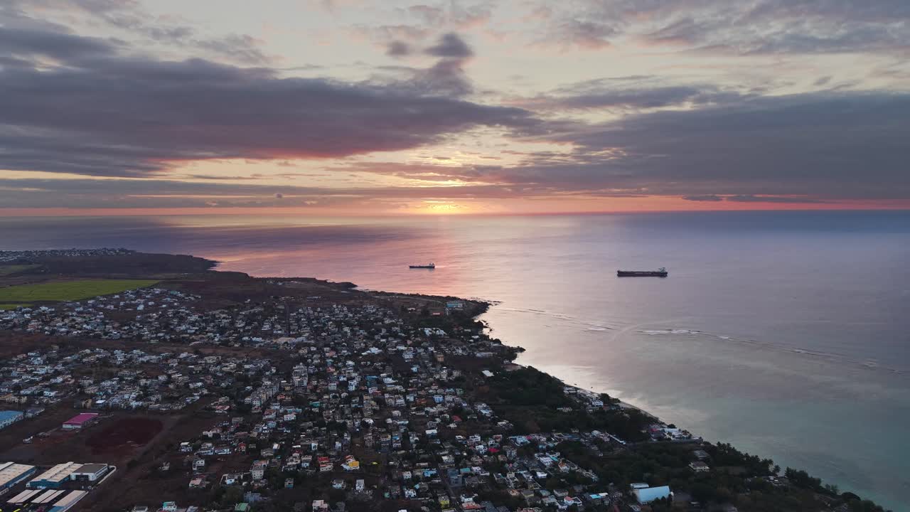 Sunset aerial view over the Mauritius coastline with anchored oil tankers and coastal towns, reflecting warm evening light across calm ocean waters
