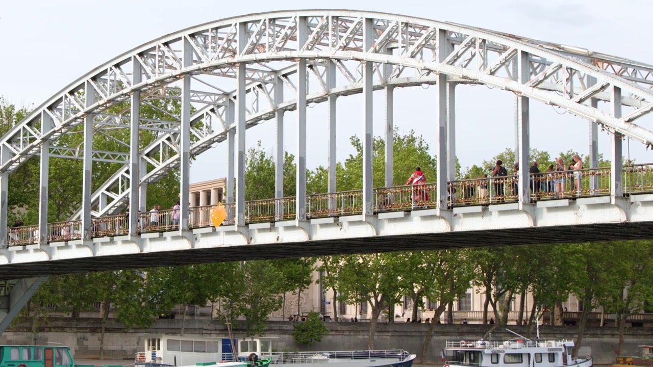 A wide shot of pedestrians crossing the white steel Debilly Footbridge in Paris, France