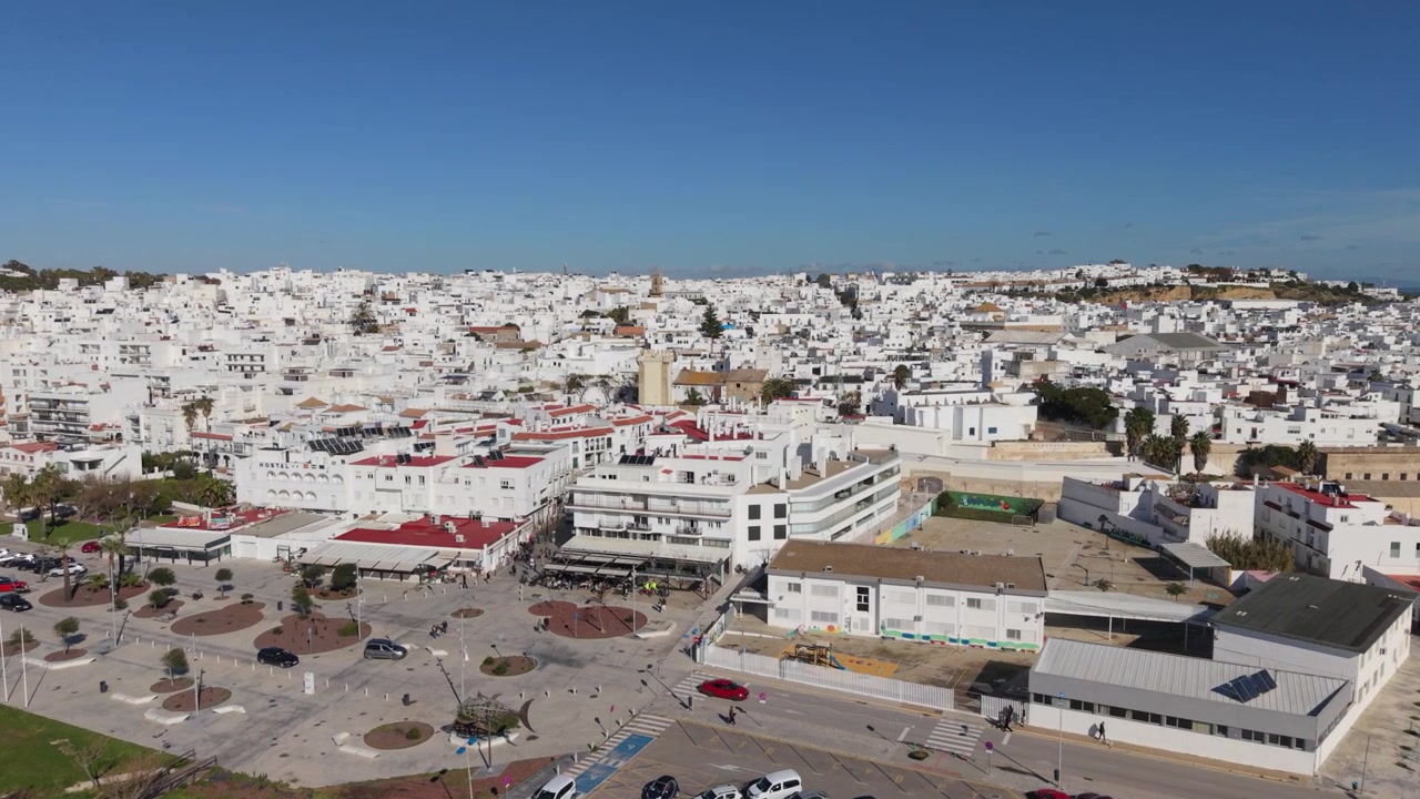 Conil de la Frontera, Cádis, Espanha. Filmagem detalhada de drone avançando sobre a orla marítima, revelando lentamente a extensão desta histórica cidade de muros brancos em um dia ensolarado com céu azul claro