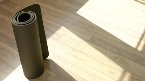 una alfombra de yoga enrollada se encuentra en el piso de madera con sombras de proyección de luz solar