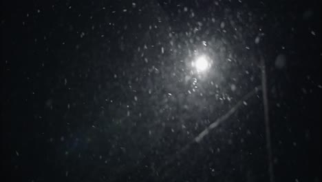 winter snowfall at night snowing on city street in street light