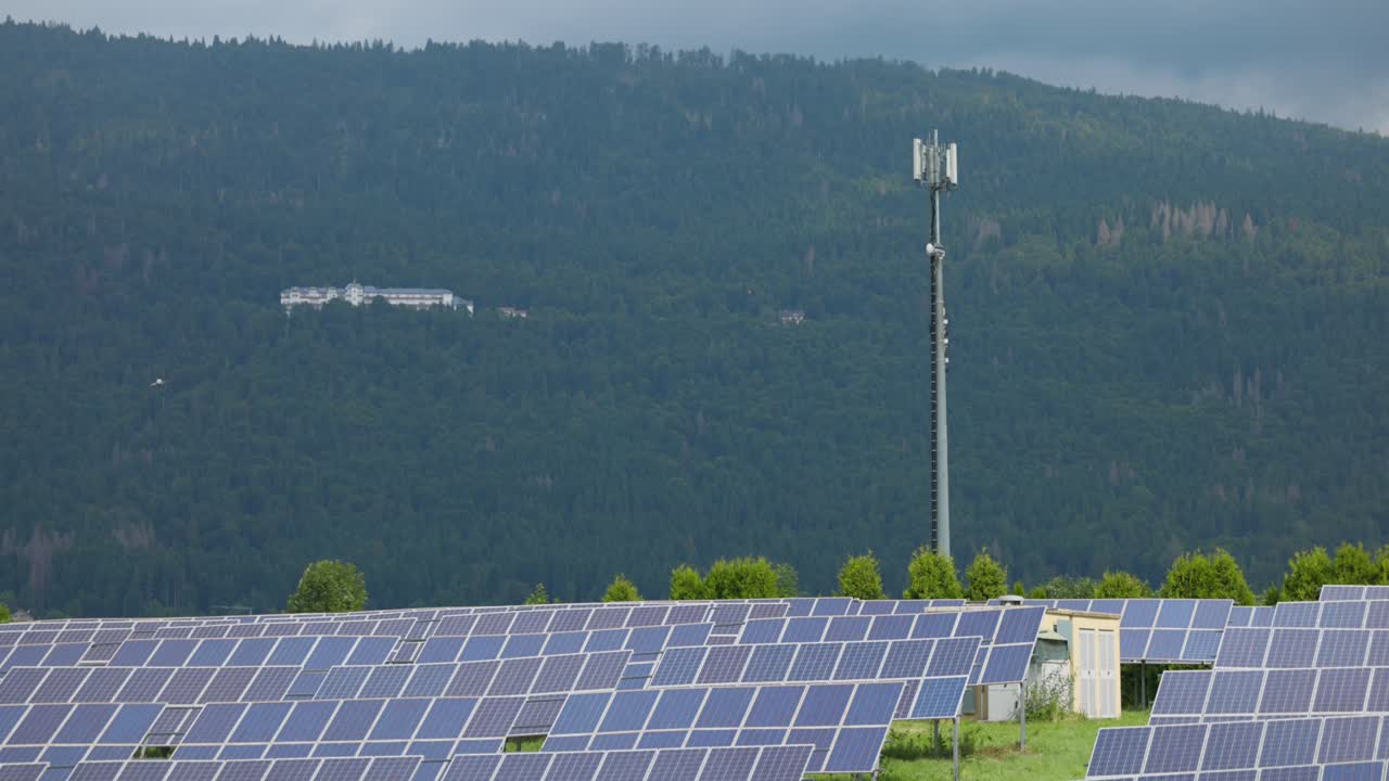 Large solar farm with photovoltaic panels. Cell tower and forested mountain in background. For renewable energy or technology content, Italy