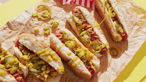 Video-of-hot-dogs-with-mustard,-ketchup-and-jalapeno-on-a-yellow-surface