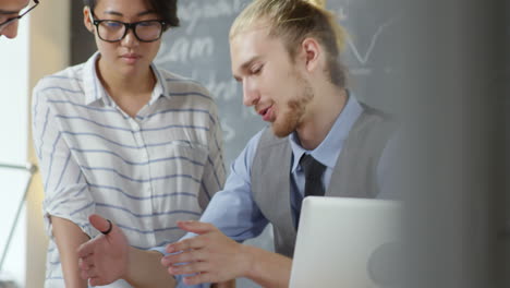 Young-Team-Of-Coworkers-Working-On-New-Project-Discussing-Details-And-Strategies-Sitting-In-Office-With-Blackboard