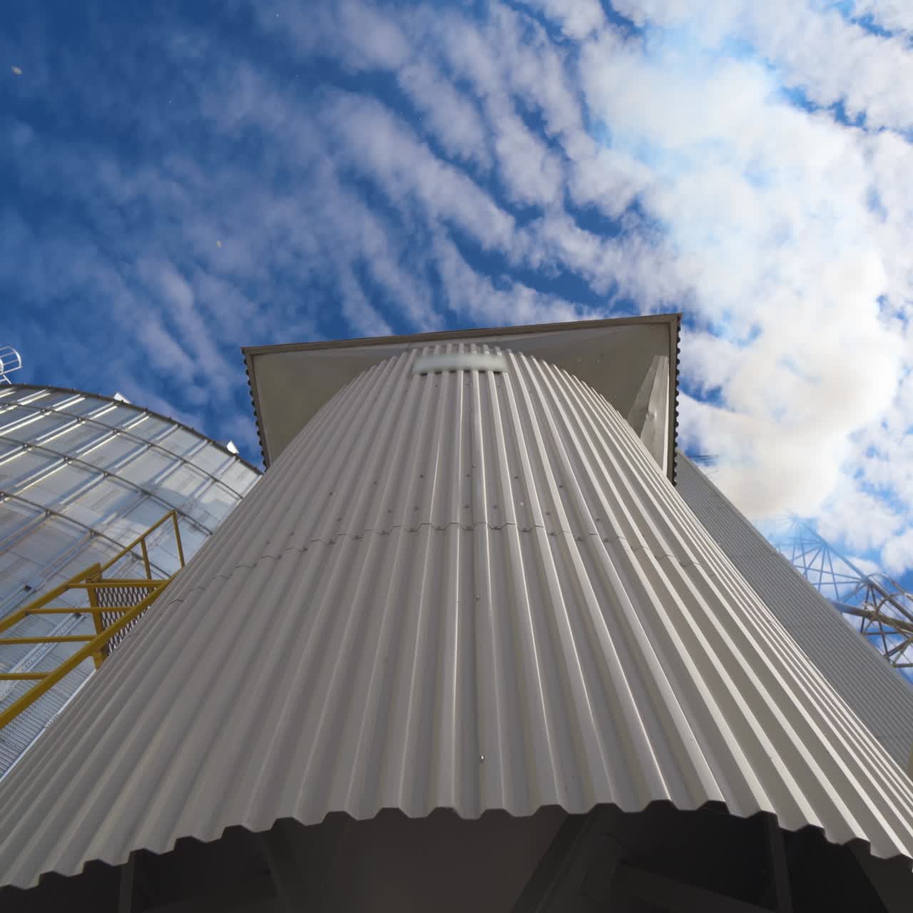 Metal construction on the modern factory. Storage tanks for processing grains on sky background. Smoke releasing from industry into the air. Close-up. Motion camera top down