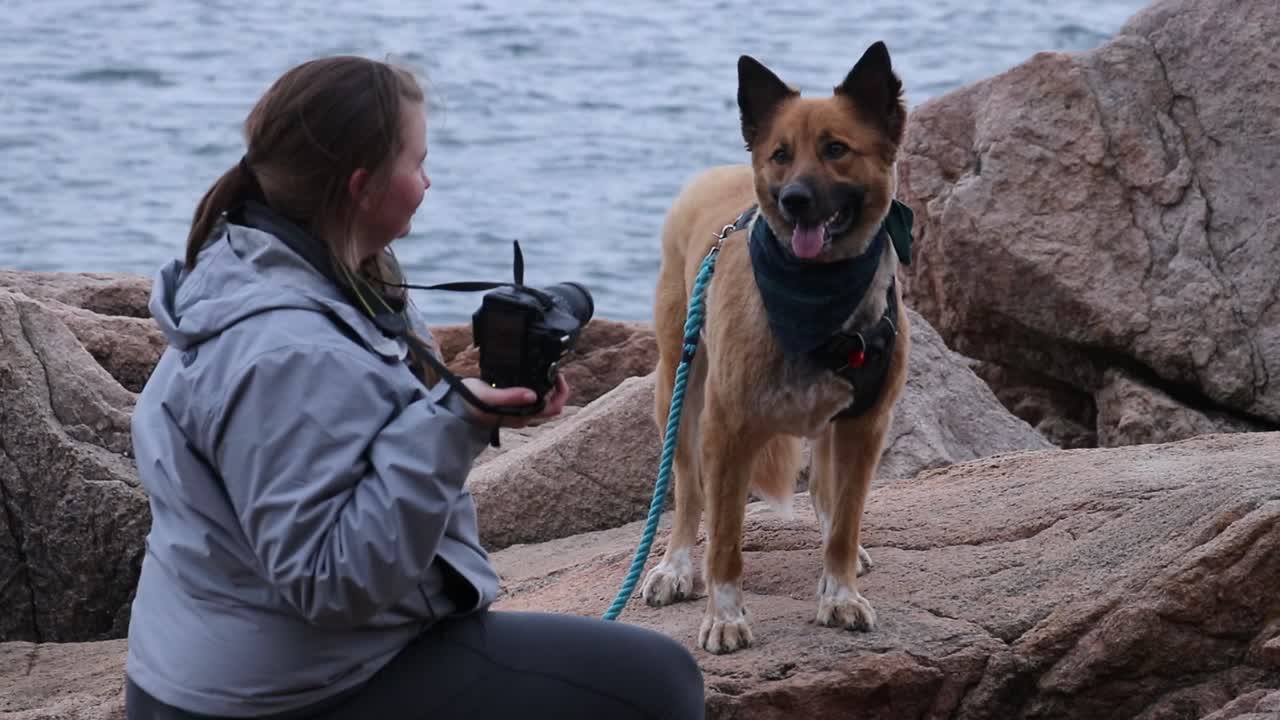 Girl takes photos of her dog with a DSLR camera on the rocky coast.