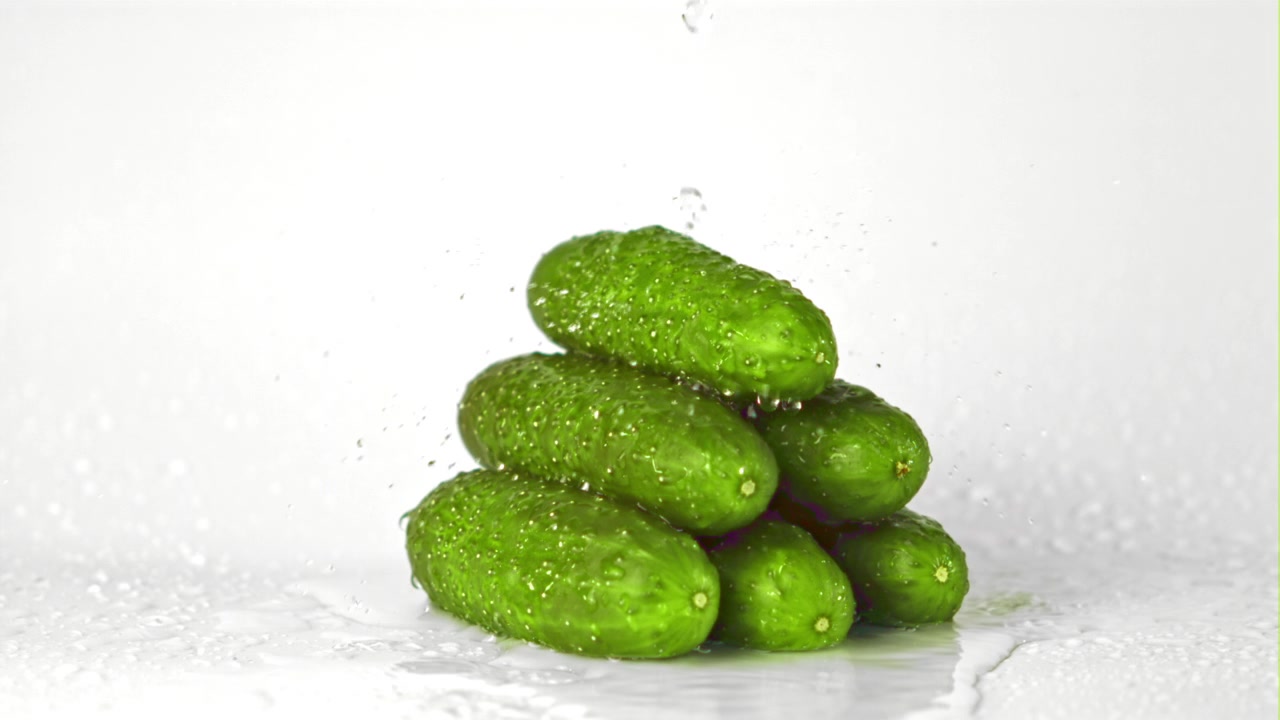 Cetrioli verdi freschi con schizzi d'acqua su sfondo bianco.