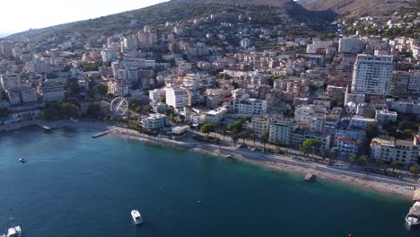 AERIAL-Flying-Further-Away-Shot-of-Sarande,-Albania-by-the-Beautiful-Mediterranean-Sea