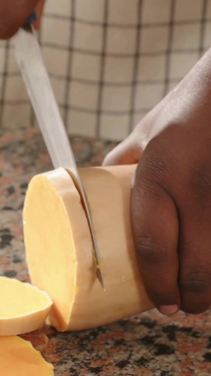 Vídeo vertical: Homem com avental colocando abóbora butternut cortada ao meio e fatiando rodelas em bancada de granito para cozinhar.