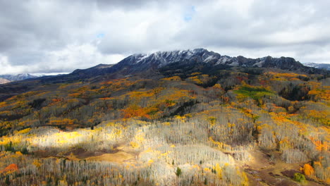 Dramatic-sunny-cloudy-autumn-Aspen-Tree-fall-colors-Kebler-Pass-aerial-cinematic-drone-snow-on-peaks-landscape-Crested-Butte-Gunnison-Colorado-early-fall-red-yellow-orange-Rocky-Mountains-backward