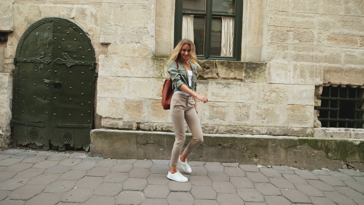 Giovane donna bionda caucasica che cammina per strada, saltando e guardando la telecamera