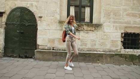 giovane donna bionda caucasica che cammina per strada mentre salta e guarda la macchina fotografica