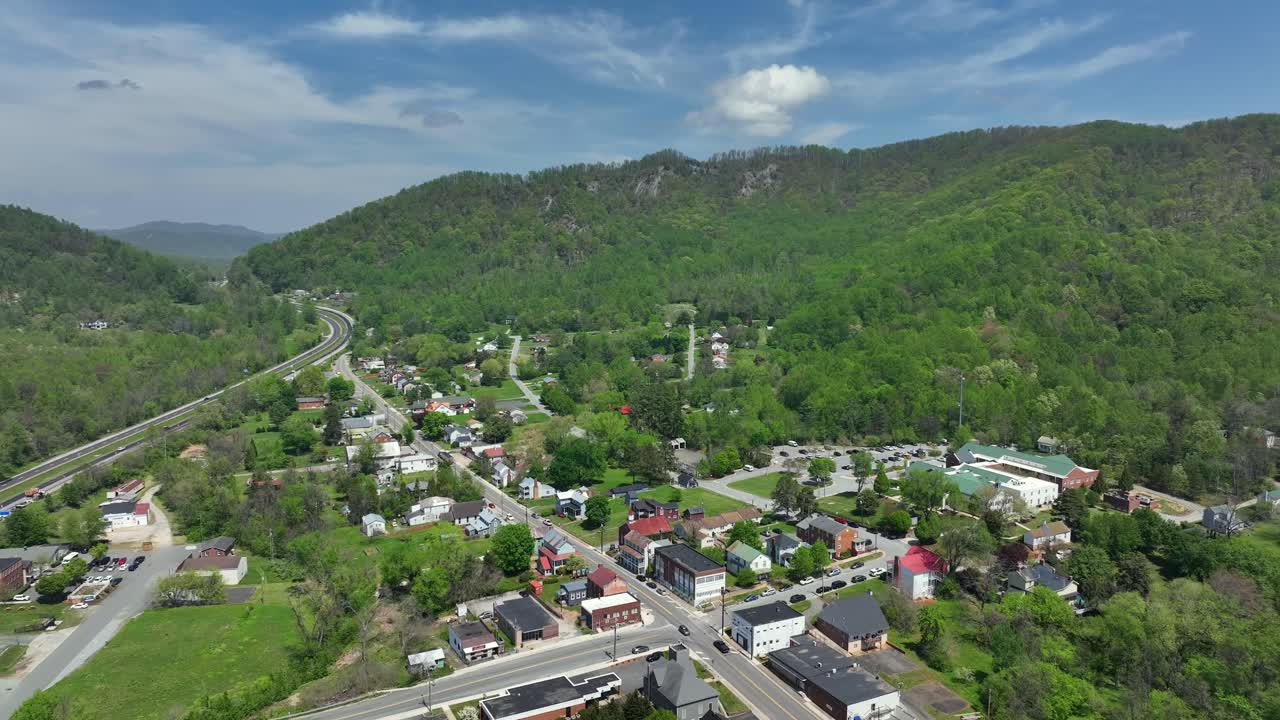 Small american town located between green mountains and highway in USA. Aerial backwards wide shot. Junction with cars in Lovingston, Virginia, America. Idyllic landscape and quiet Atmosphere.