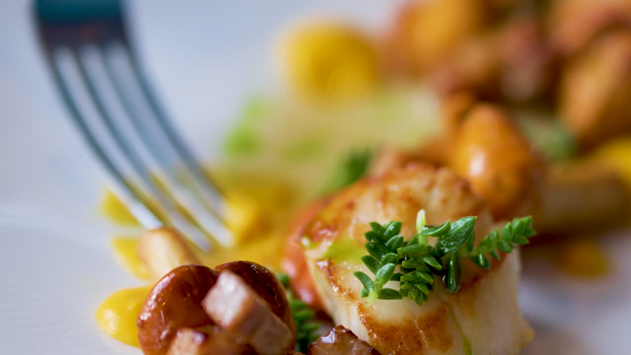 A gourmet seafood scallop dish is delicately eaten with a fork in a fine dining setting, captured in a shallow depth-of-field close-up with natural lighting