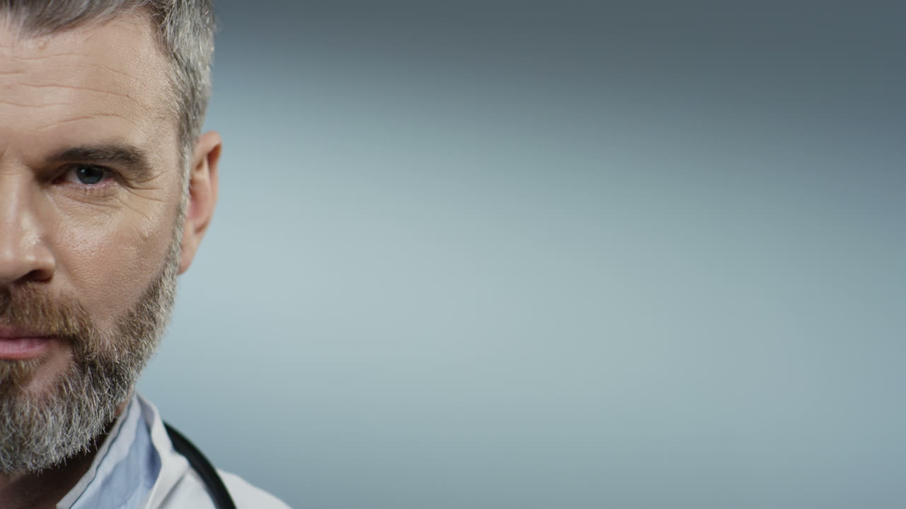 nahaufnahme des halben gesichts des ernsthaften arztes mit bart, der direkt in die kamera blickt