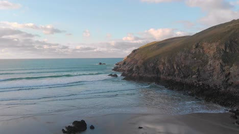 The-stunning-aerial-shot-of-Perran-Sands-during-sunset,-surfers-are-in-the-water-waiting-to-catch-a-perfect-wave