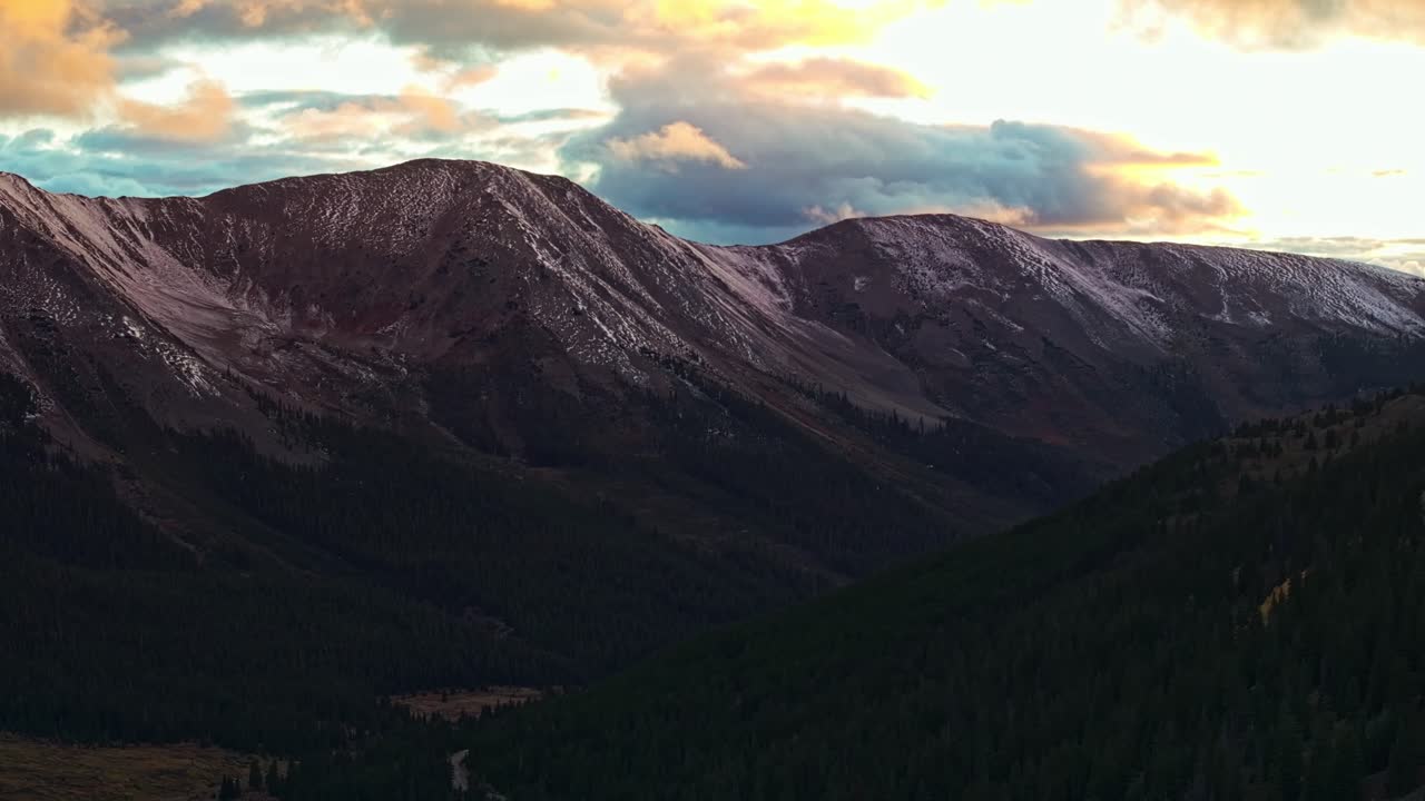 Drone view soaring over a winding road through green valleys and snow-capped mountains in Independence Pass