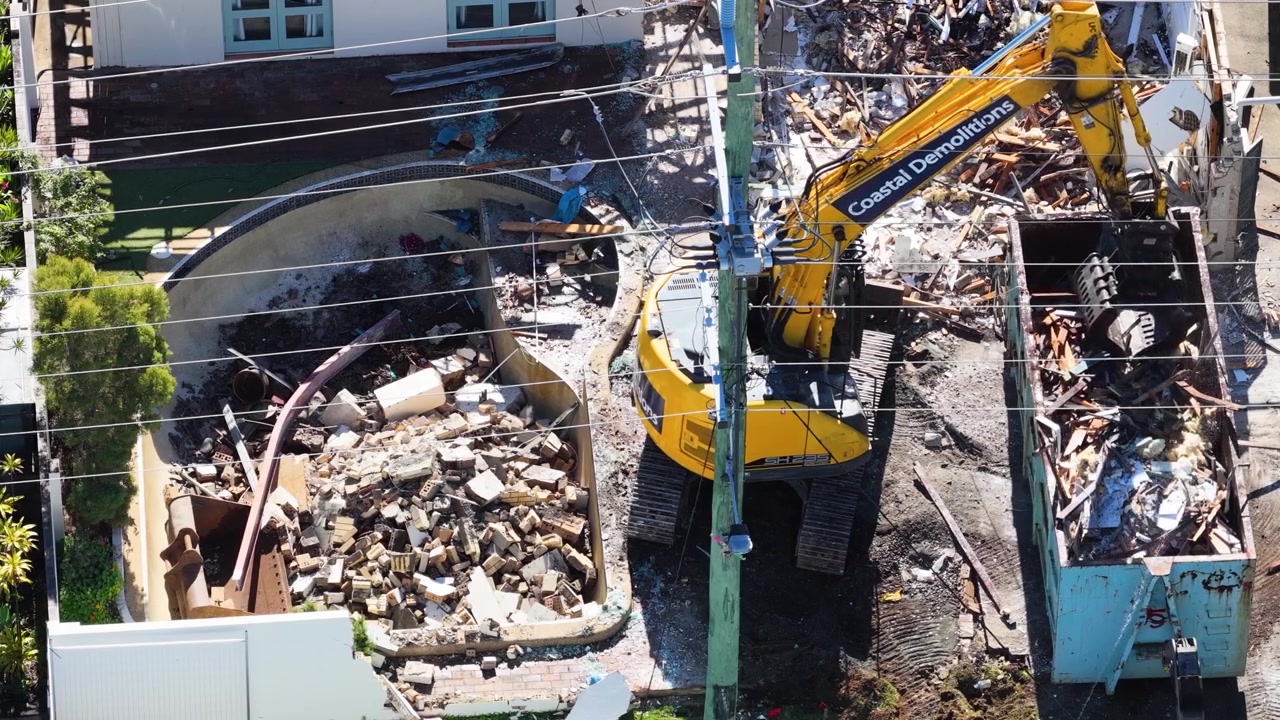 Pelleteuse jaune démolissant un bâtiment résidentiel et chargeant des débris dans une benne