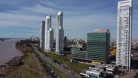 Wunderschöner-Architektonischer-Blick-Auf-Rosario-Aus-Einer-Drohne-An-Einem-Sonnigen-Tag-Entlang-Der-Küste-Von-Paraná,-Während-Autos-Die-Straße-Am-Fluss-überqueren