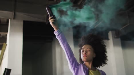 mixed race woman holding green flare standing in an empty building