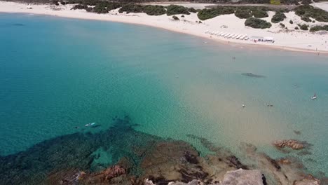 Drone-Aterriza-En-La-Pequeña-Isla-Frente-A-La-Hermosa-Playa-De-Chia-En-El-Sur-De-Cerdeña,-Clima-Soleado