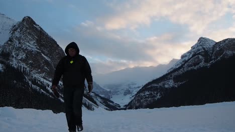 man walking on frozen lake with mountains in background