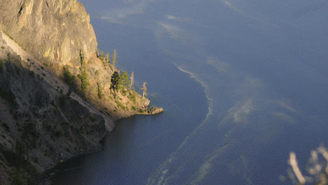 static shot looking down at the crystal blue water in crater lake oregon with the steep mountain ridge meeting the water line