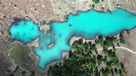 Cinematic-drone-shot-of-turquoise-colored-water-in-the-mountains-at-Naltar-Valley-in-Pakistan,-slowly-descending-aerial-shot