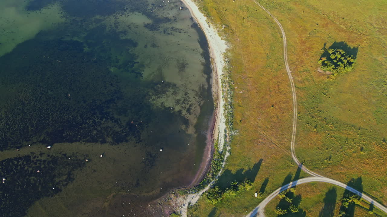 vista de sandbybadet, öland en suecia compuesta de campo verde y aguas transparentes durante el día soleado - toma aérea