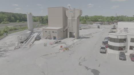 Concrete-plant-with-2-workers-walking,-trucks,-and-office-revealed-in-panning-shot,-Massachusetts