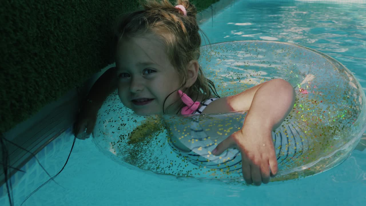 사랑스러운 작은 소녀가 이 좋은 날에 부풀어오르는 원과 함께 수영장에서 수영하고 있습니다.