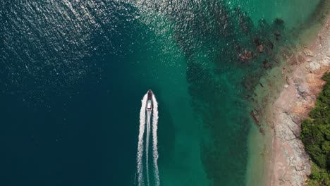 Aerial-drone-tops-down-motorboat-sailing-blue-turquoise-sea-bay-in-Japan-beach-with-white-sand-rocks-and-cliffs,-natural-paradise-in-Japanese-Wakayama