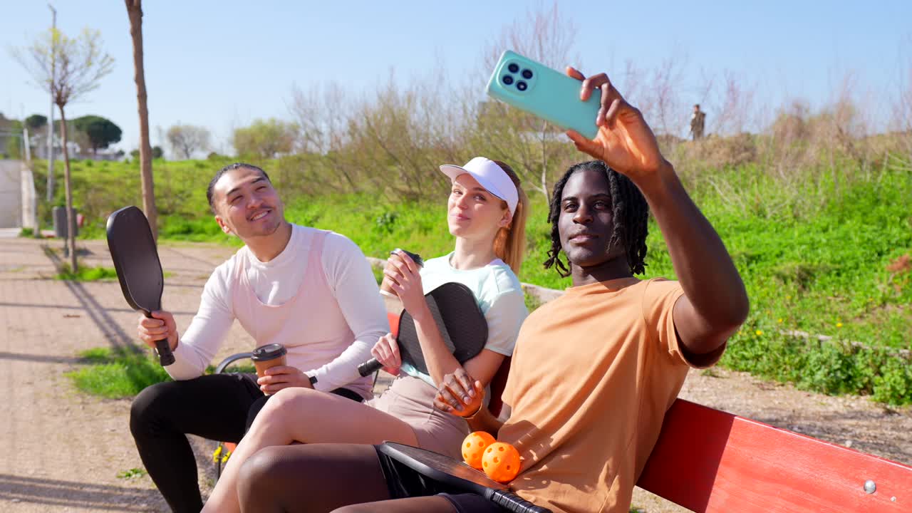 Amici di diverse origini che si scattano un selfie e si rilassano su una panchina del parco