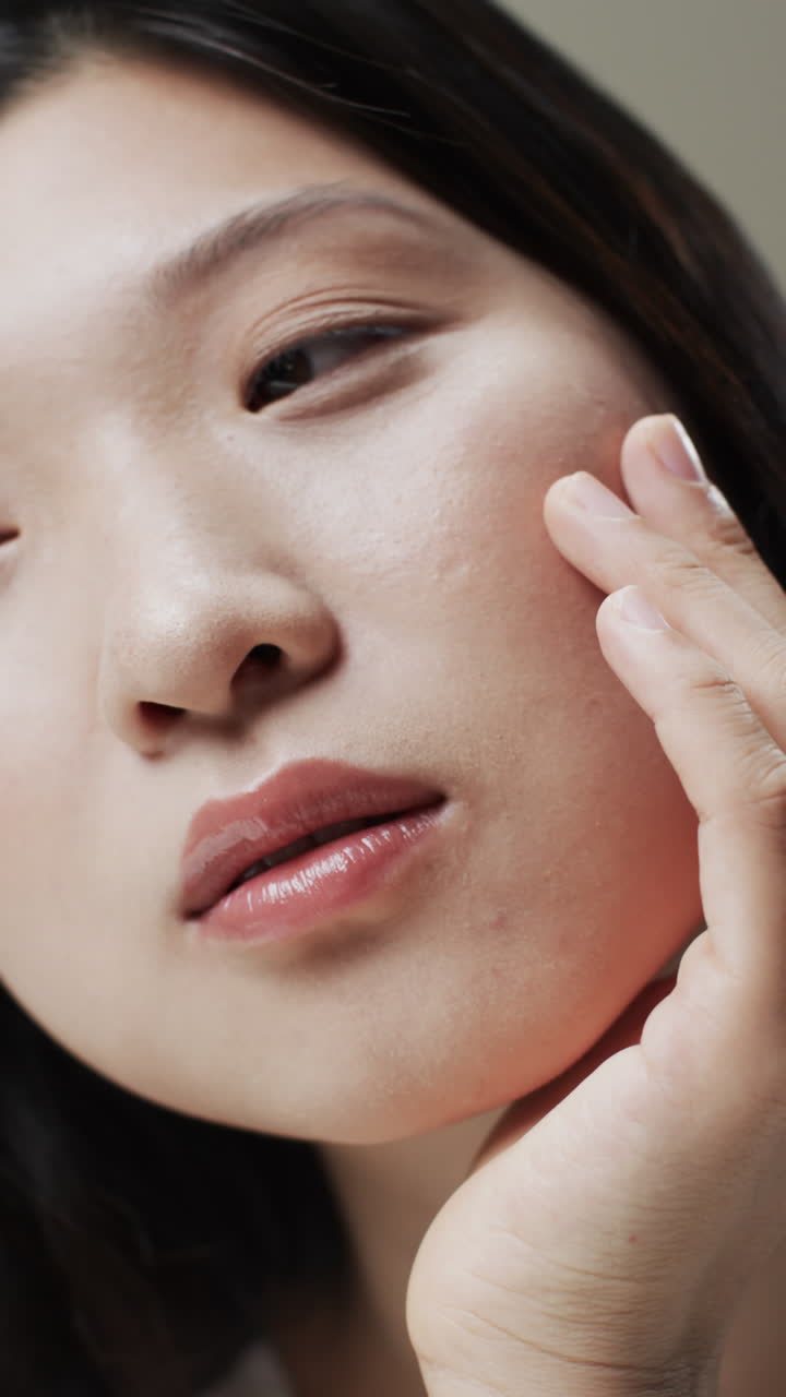 Vertical video of asian woman with black hair and make up touching face, copy space, slow motion
