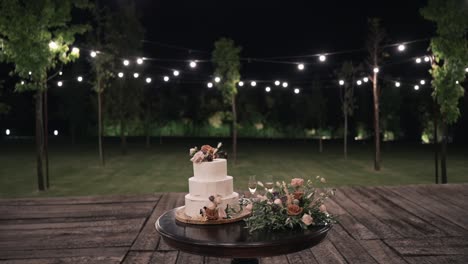 Pastel-De-Bodas-En-Una-Mesa-Al-Aire-Libre-Por-La-Noche-Con-Luces