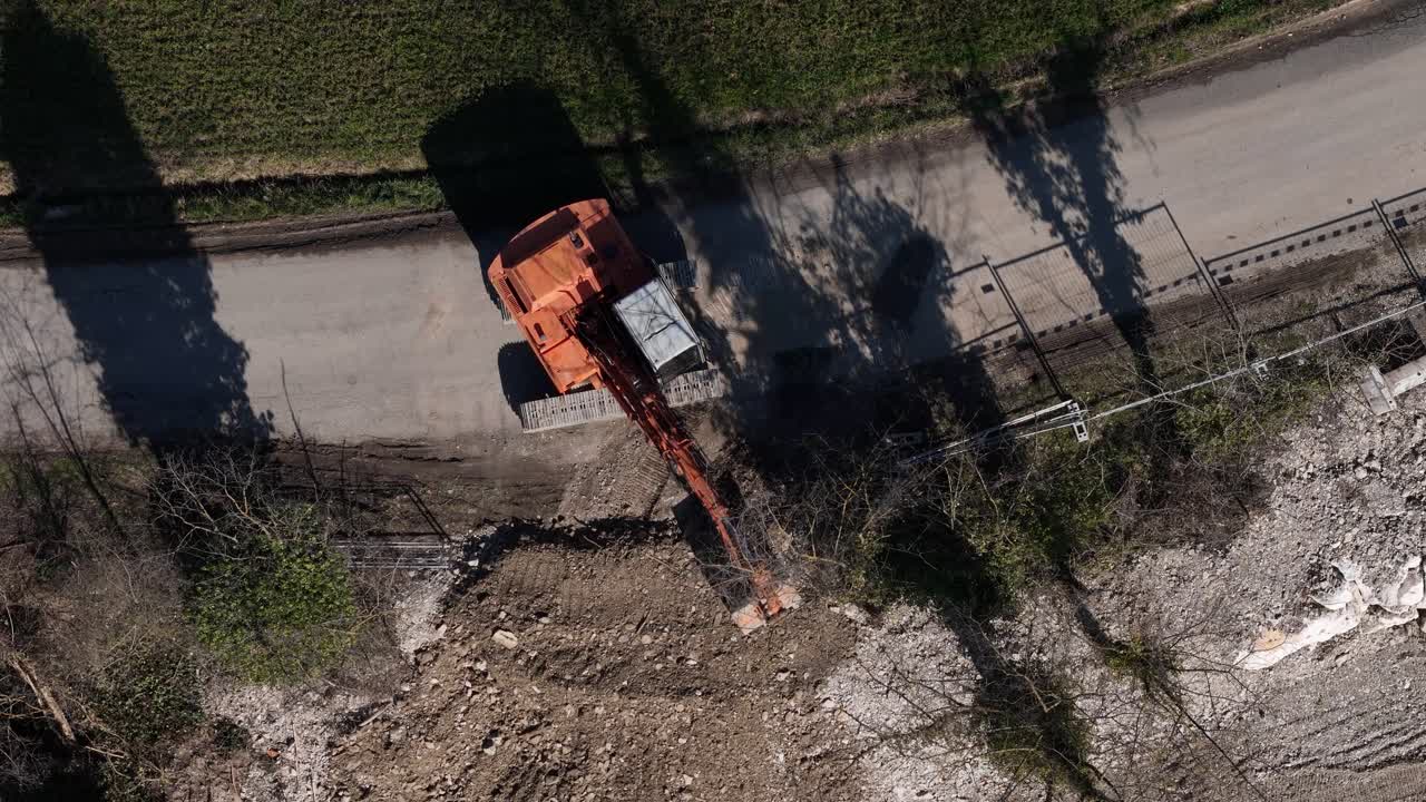 Luftfoto fra oven af gravemaskine, der graver en drænkanal ved siden af en landevej til vandforvaltning og infrastrukturvedligeholdelse